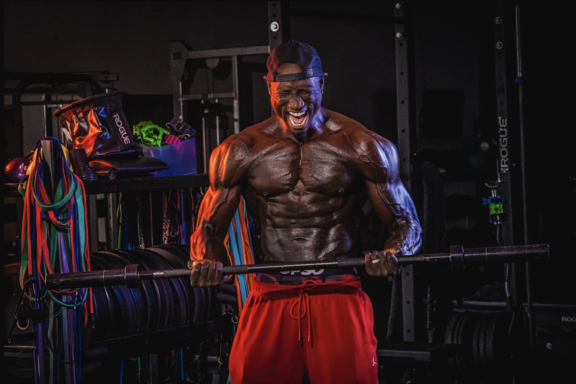 Coach JR curling a barbell in a gym lined with resistance bands